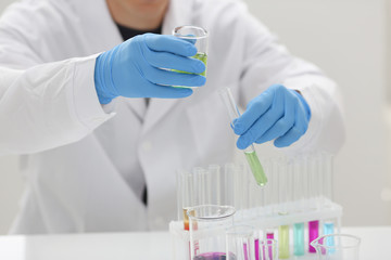 A male chemist holds test tube of glass in his hand overflows a liquid solution of potassium permanganate conducts an analysis reaction takes various versions of reagents using chemical manufacturing.