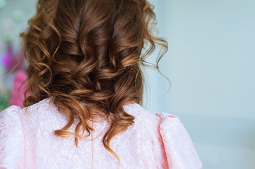 curly hair in a hairstyle to the shoulders of a girl in a pink dress back view