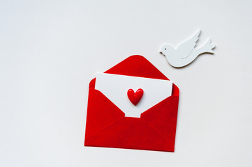 Red envelope with blank postcard and heart on white background. Dove brought the good news. Valentine's Day concept. Minimalism, copy space, top view.