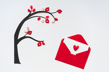 Tree of kisses with red envelope and blank postcard. Tree with leaves in shaped of lips on white background for Valentine's Day card. Minimalism, copy space, top view.