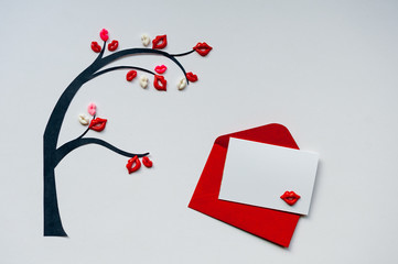 Tree of kisses with red envelope and blank postcard. Tree with leaves in shaped of lips on white background for Valentine's Day card. Minimalism, copy space, top view.