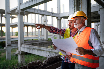 Two satisfied engineers talking at building site with construction structure in background