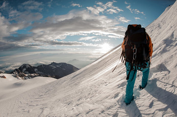 Naklejka premium Rear view guy with hiking equipment climbing on the snow on the mountain hill