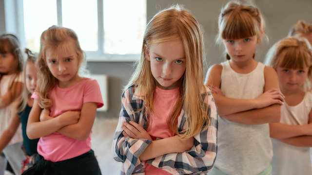 Hip hop dancers. Group of cute little girls keeping arms crossed and making serious faces while having a choreography class in the dance studio