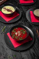 Set of different soups. Chicken broth, red borsch, lentil with bacon, mushroom cream soup. Delicious fragrant first courses. Festive table with delicious food on black boards.