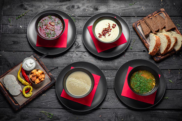 Set of different soups. Chicken broth, red borsch, lentil with bacon, mushroom cream soup. Delicious fragrant first courses. Festive table with delicious food on black boards.