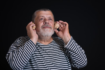 Low key portrait of bearded senior man listening sounds of sea shells