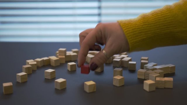 Young female hand with a red manicure in sweater changing green wooden block for red between other mono coloured blocks and put it in the middle of footage. Closeup video where girl playing with the w