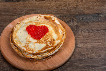 Round pancakes pancakes, cawith a heart in the middle of red caviar, lie on the board. Close-up, top view, Flat Lay, Copy space, place for text. Shrovetide, East Slavic traditional holiday of Ukraine.