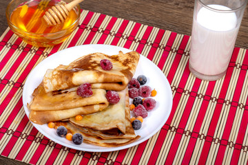 Fototapeta na wymiar A plate with fried pancakes, folded triangles, a bowl of honey and a glass of fresh milk on a wooden dark background. Angle view, close-up, Copy space. Shrovetide, East Slavic traditional holiday