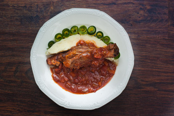 lamb shank cooked in rich tomato sauce, served with potato purée and cucumber slices 
