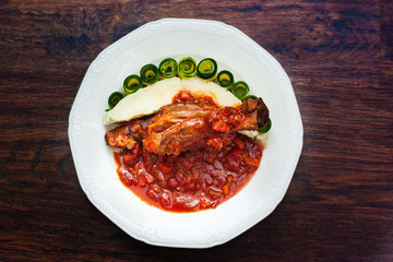 lamb shank cooked in rich tomato sauce, served with potato purée and cucumber slices 