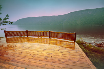 Wooden wet deck on a lakeshore. Rocky shore of the mountain lake in rainy autumn morning. Beautiful nature Norway.