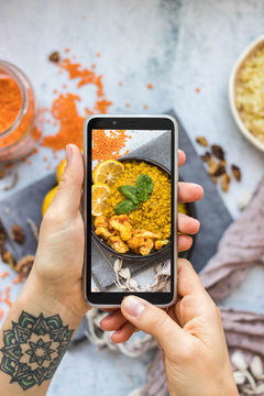 Woman take picture of vegan food with phone at her kitchen. Hand make a closeup smartphone photo of Indian masala lentil for blogging or social media content. Vegetarian healthy food.