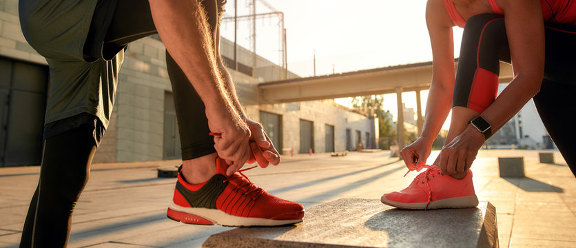 Active morning. Close up photo of two people in sport clothes tying shoelaces before running together outdoors