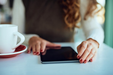 Close up of an Attractive young curly brunette enjoying her coffee/tea and working on tablet	