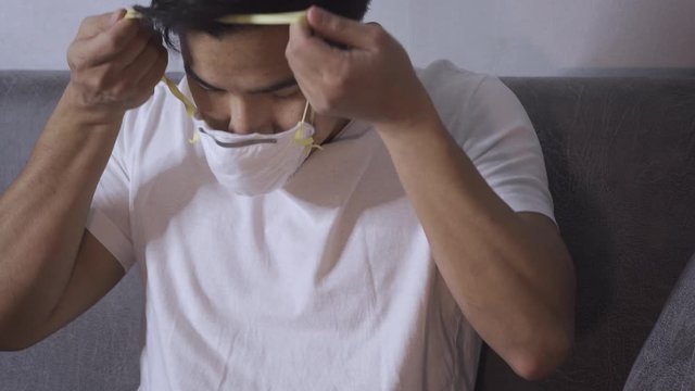 4k Asian young woman put on white mask, sitting in living room, white zip up shirt, medical protective mask, h1n1, ebola, mers, sika, virus spreading, health care concept, side view, transmit disease
