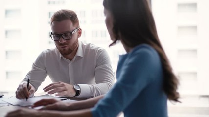Two young colleagues man and woman team discuss new business project at workplace in the light modern office room against large window. Tracking shot in slow motion.