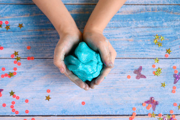 a little girl hands making slime herself on blue wooden background