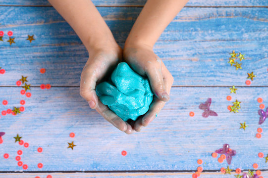 a little girl hands making slime herself on blue wooden background
