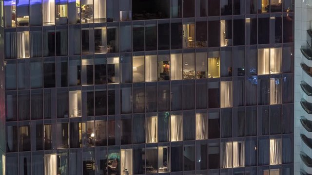 Night view of office and apartment building timelapse. High rise skyscraper with blinking windows with people moving inside. Aerial view from above. Zoom out