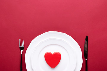 Minimal table setting with heart for Valentine's Day on red background. Top view, concept of eating...