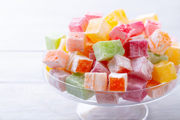 Assortment of Turkish delights on a glass stand. White wooden background. Close up.