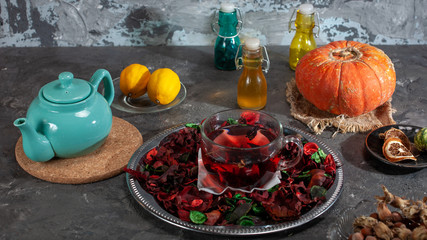 Red Hot Hibiscus tea in a glass mug on a wooden table among rose petals and dry tea custard with metallic heart