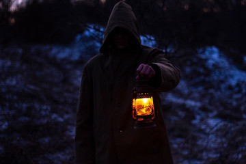 a man with an old glowing lantern in a raincoat in a dark forest . Silhouette of a cult, a person...