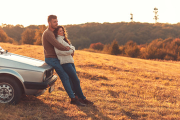 Beautiful young couple enjoying time together outdoor sitting on meadow leaning on old fashioned...