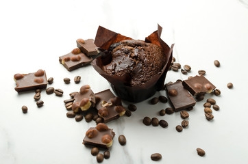 Chocolate muffin, pieces of choclte with hazelnuts and coffee beans on the white table