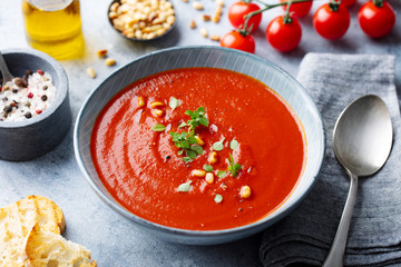 Tomato soup with fresh herbs and pine nuts in a bowl. Grey stone background. Close up.