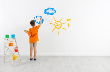 Little child painting cloud on white wall in room
