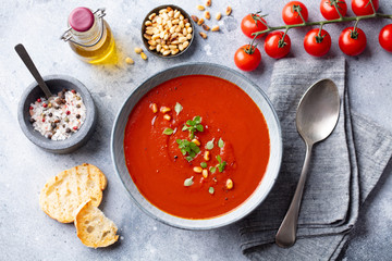 Tomato soup with fresh herbs and pine nuts in a bowl. Grey stone background. Top view.