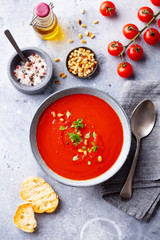 Tomato soup with fresh herbs and pine nuts in a bowl. Grey stone background. Top view.