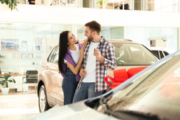 Happy couple with car key in modern auto dealership