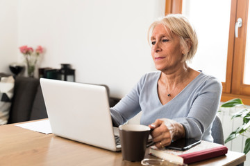 retired woman holding a cup of coffee  working at home