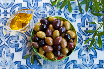 Assortment of fresh olives on a plate with olive tree brunches. Blue textile background. Top view.