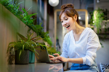 Young Asian woman using laptop to communicate or typing mail to respond client while sitting at coworking space. Startup entrepreneur running online business, working from network technology.