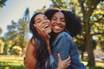 Muurstickers Close up lifestyle portrait of diverse multiracial happy best friends hugging each other and laughing in the park © StratfordProductions