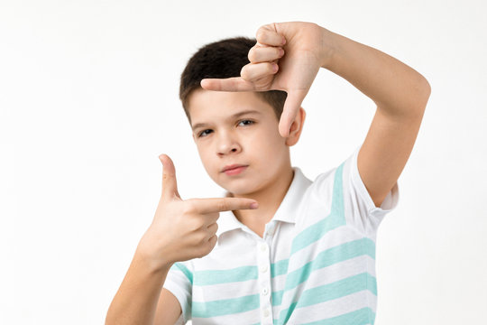happy funny little child boy in striped t-shirt making hands photo frame gesture on white background. facial expression