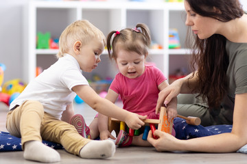 Naklejka premium Preschooler children playing with educational wooden toys at kindergarten or daycare center. Toddlers with teacher in nursery.