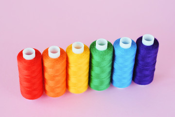 LGBT flag colors creative concept. Rainbow color sewing treads on the pink pastel  background. Sewing accessories.