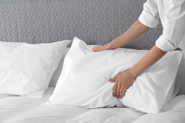 Woman fluffing soft pillow in bedroom, closeup