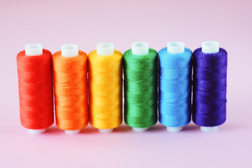 LGBT flag colors creative concept. Rainbow color sewing treads on the pink pastel  background. Sewing accessories.