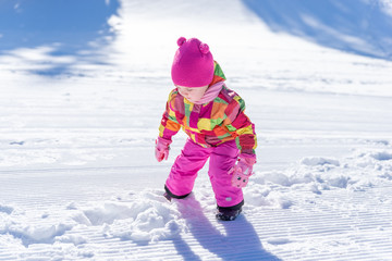 Little girl is playing in the snow. Girls wear a pink hat, scarf, jacket, gloves and a suit. Concept of winter vacation