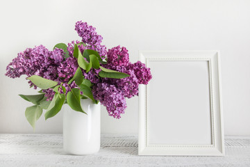 Bouquet of purple lilac flowers and white photo frame on light board. Space for text.