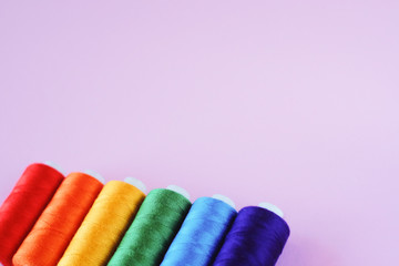 LGBT flag colors creative concept. Rainbow color sewing treads on the pink pastel  background with the empty space for text.