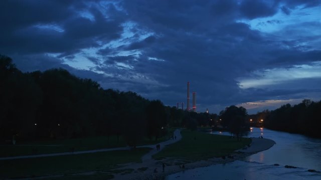 Munich nature at dramatic dusk: autumn in park of tourist Bavarian city. View of Isar river, trees and St Maximilian church from Reichenbach Bridge. Munchen, Bavaria, Germany. Camera horizontal pan
