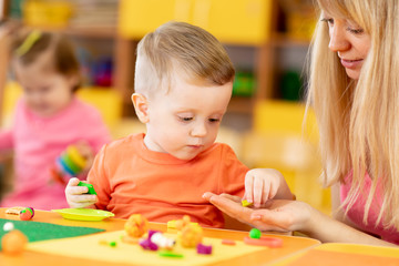 Teacher with babies in creche. Kids play clay in kindergarten